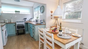 A kitchen with a dining table set for two, a stove, oven, and a sink. - The Cottage (Swanage)