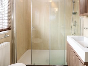 Een moderne badkamer met een douchecabine van glas, een witte wastafel en houten kastjes.