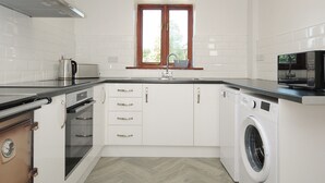 A modern kitchen with white cabinets, a built-in oven, a microwave, and a washing machine. - West Lee (Bude)