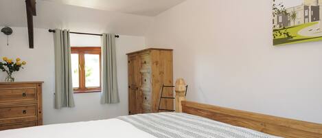 A bedroom with a bed, a wooden wardrobe, a window with curtains, a hanging light fixture, and a wall-mounted poster.
