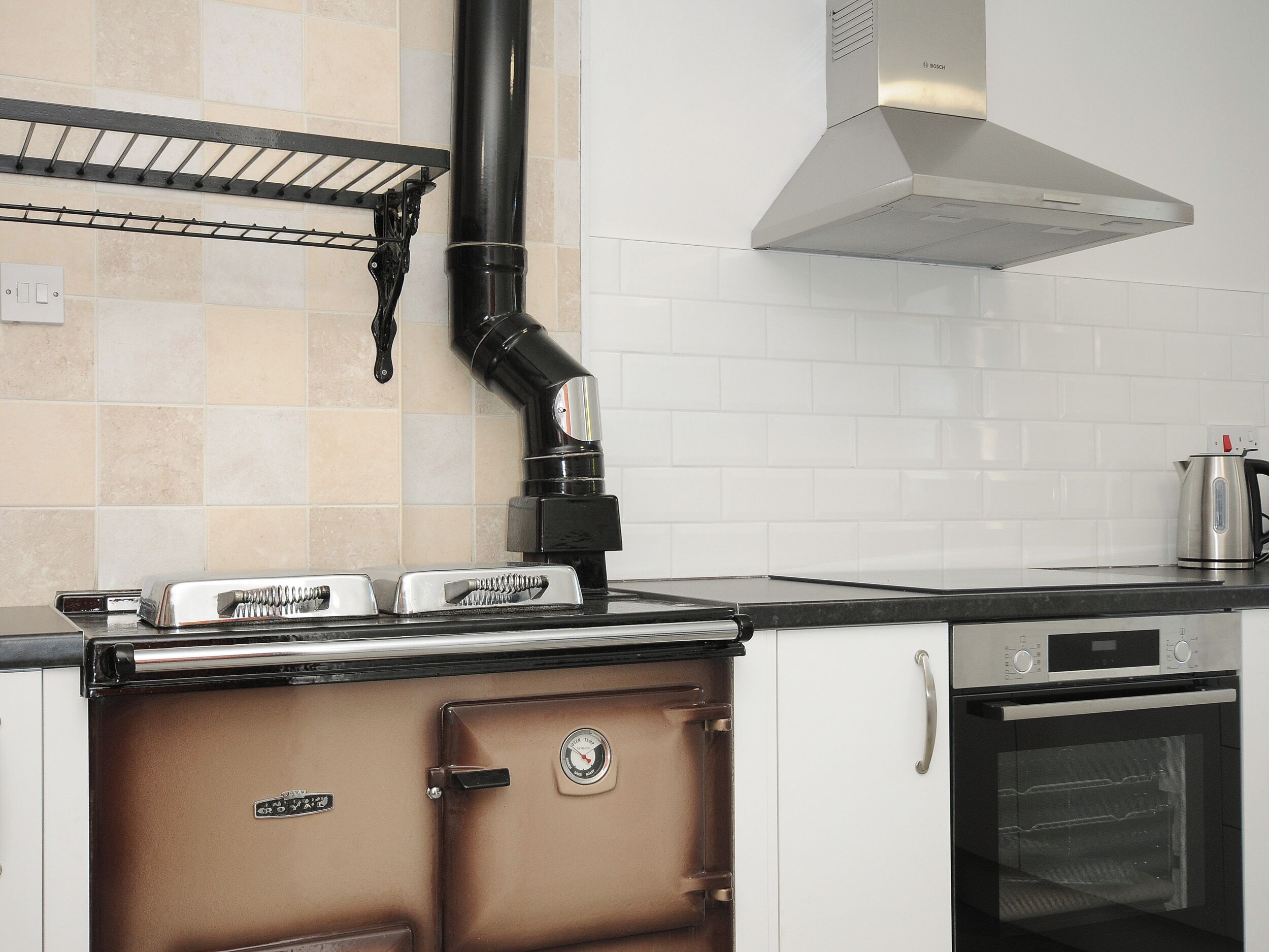 A kitchen with a built-in oven, a stainless steel range hood, and a kettle on the countertop.