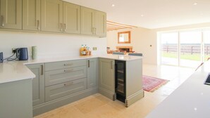 A modern kitchen with light grey cabinets, a central island, and a large sliding glass door leading to a patio. - Daniels Farmhouse (Worcester)