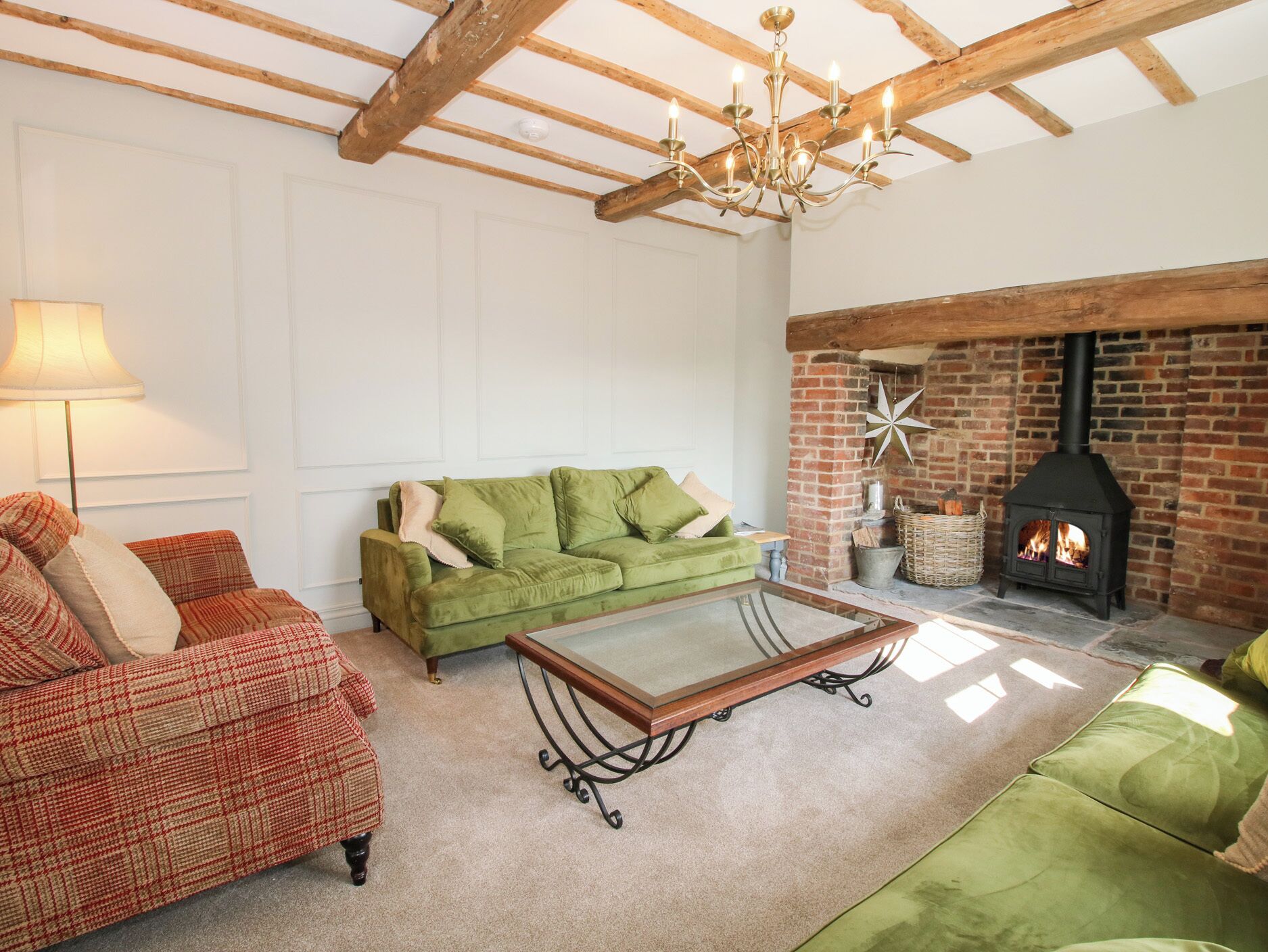 A cozy living room with a green sofa, a red patterned armchair, a glass-top coffee table, and a brick fireplace.