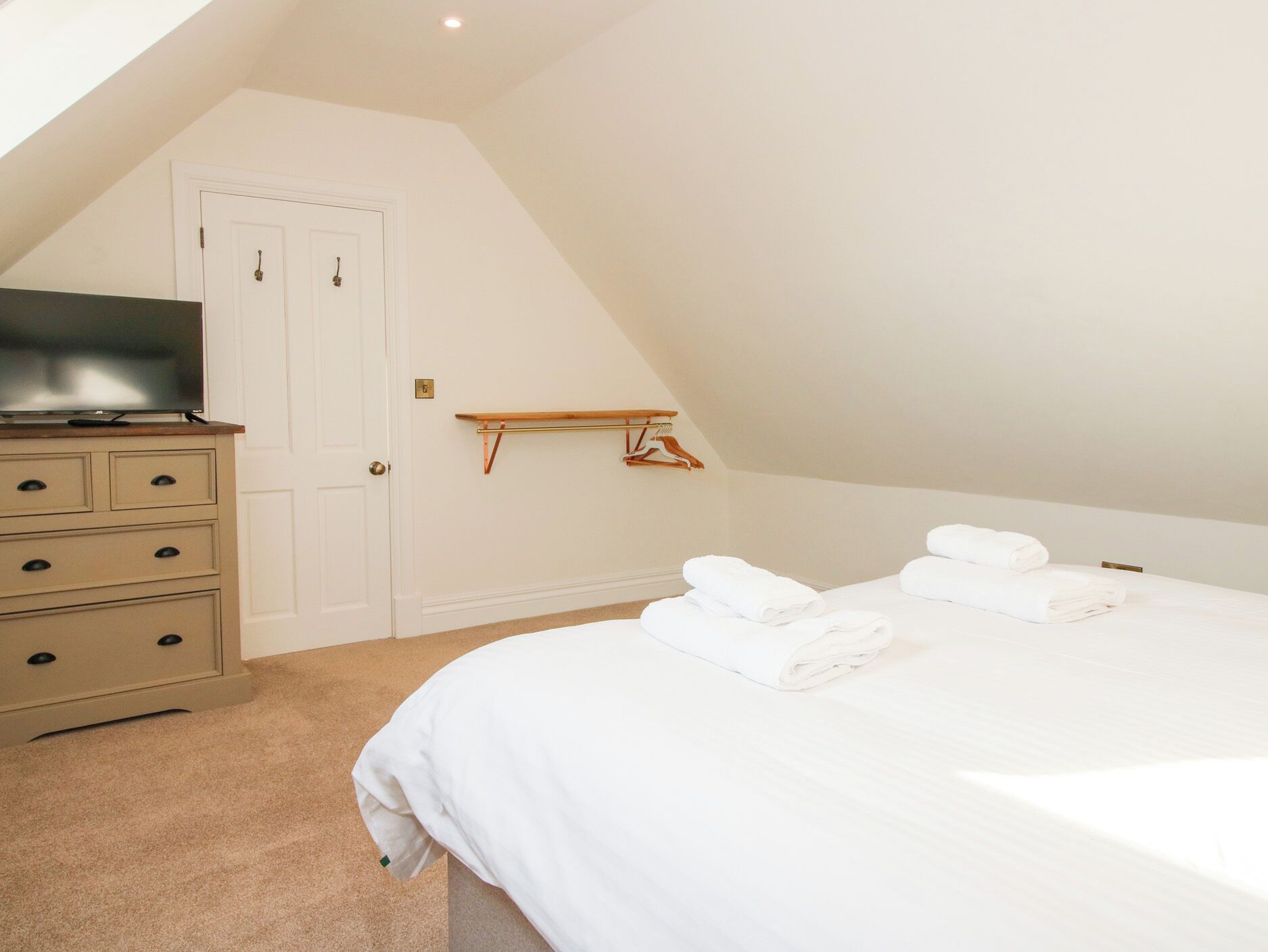 A bedroom with a bed, a dresser, a television, and a hanging rack.
