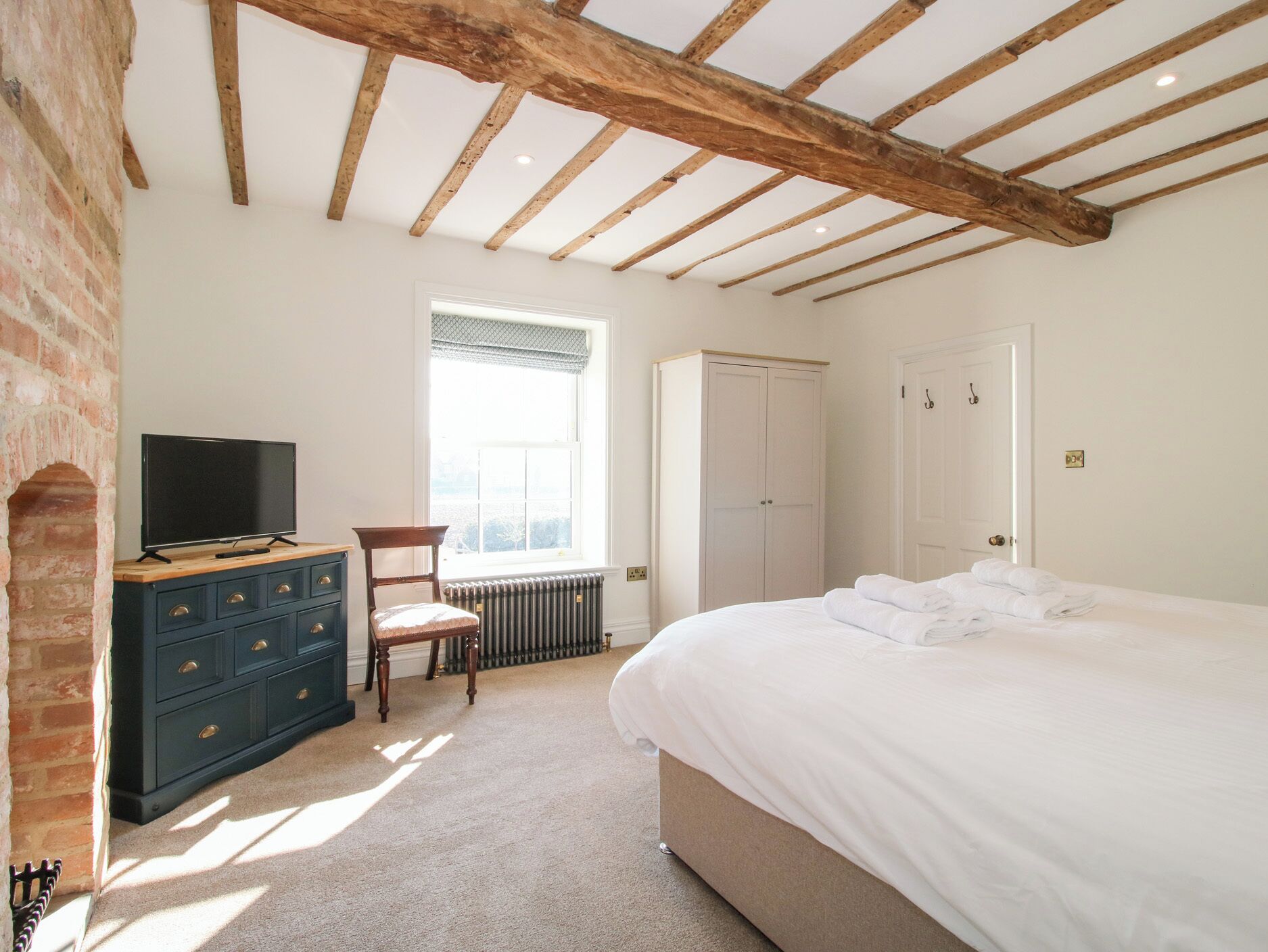 A bedroom with a bed, a dresser, a chair, a television, and a wardrobe.