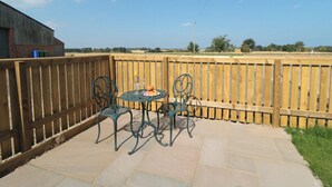 Une terrasse avec deux tables et chaises en métal, une clôture en bois et une vue sur la campagne.