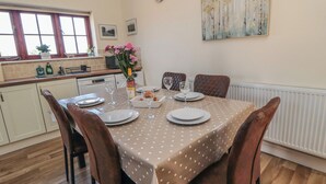 Un coin repas avec une table dressée pour quatre personnes, une horloge au mur et une fenêtre avec des rideaux.