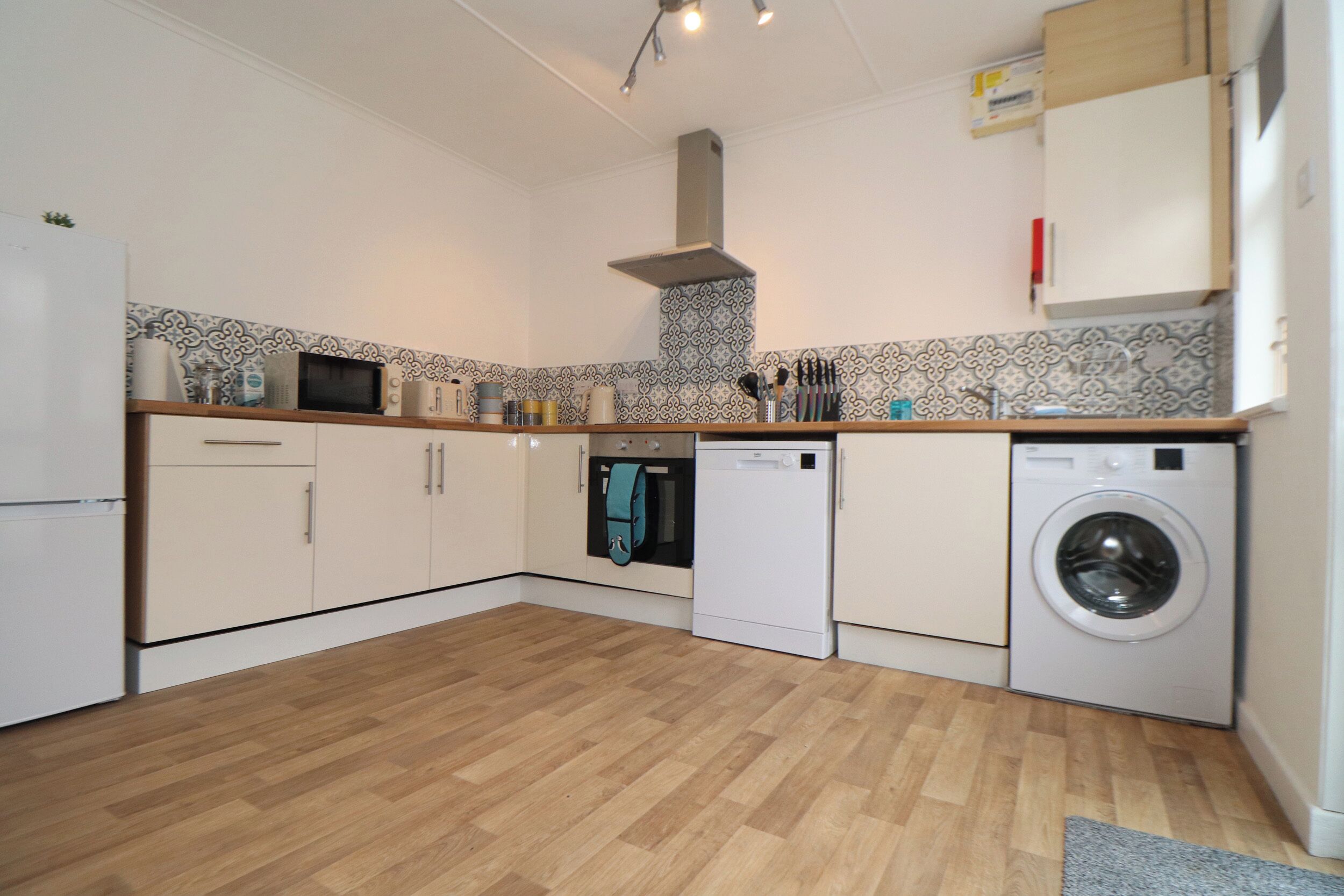 Une cuisine moderne avec un plancher en bois, des armoires blanches, un four à micro-ondes, un four, un lave-vaisselle et un lave-linge.