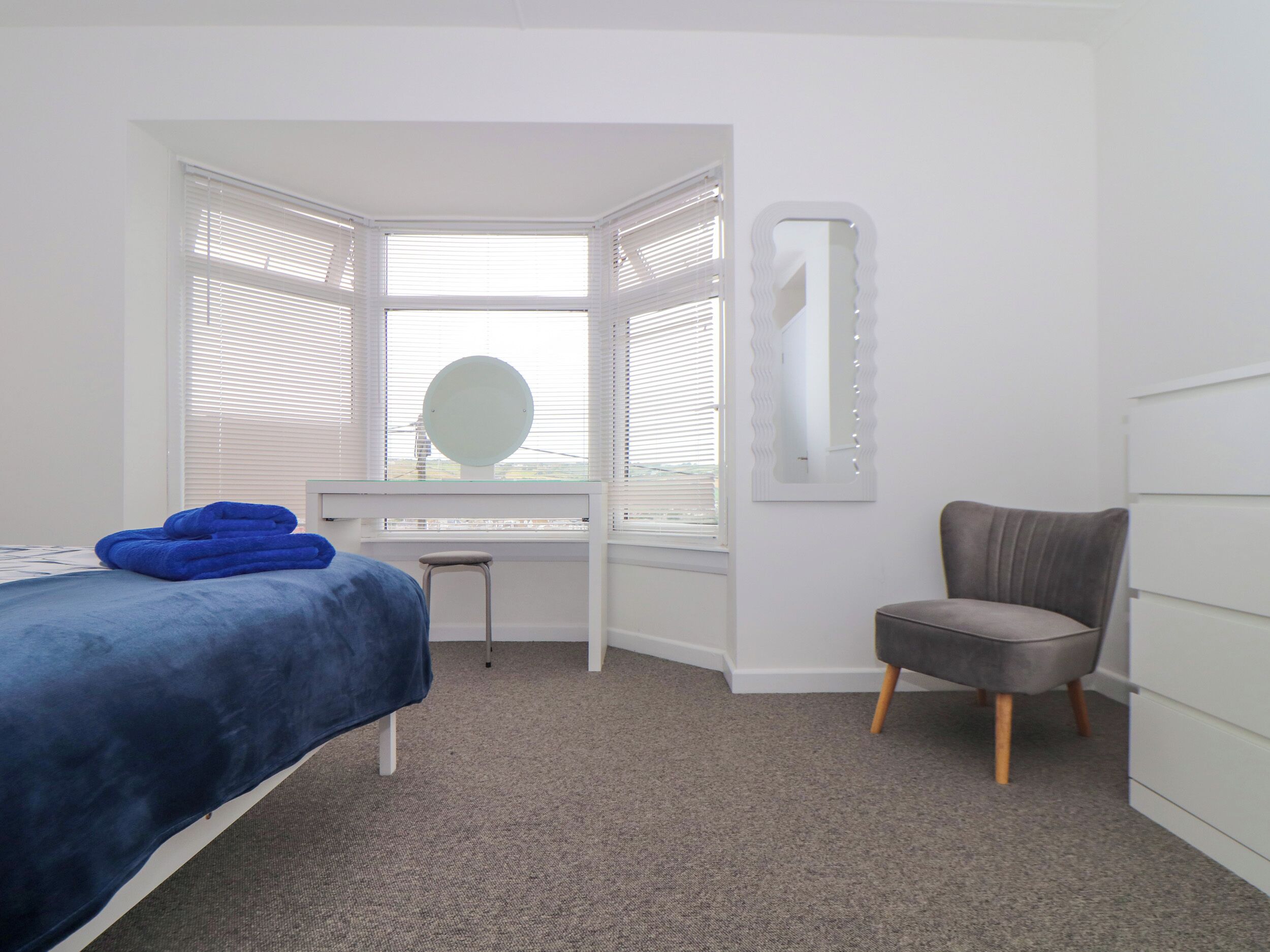 A bedroom with a bed, a desk, a chair, and a window with blinds.