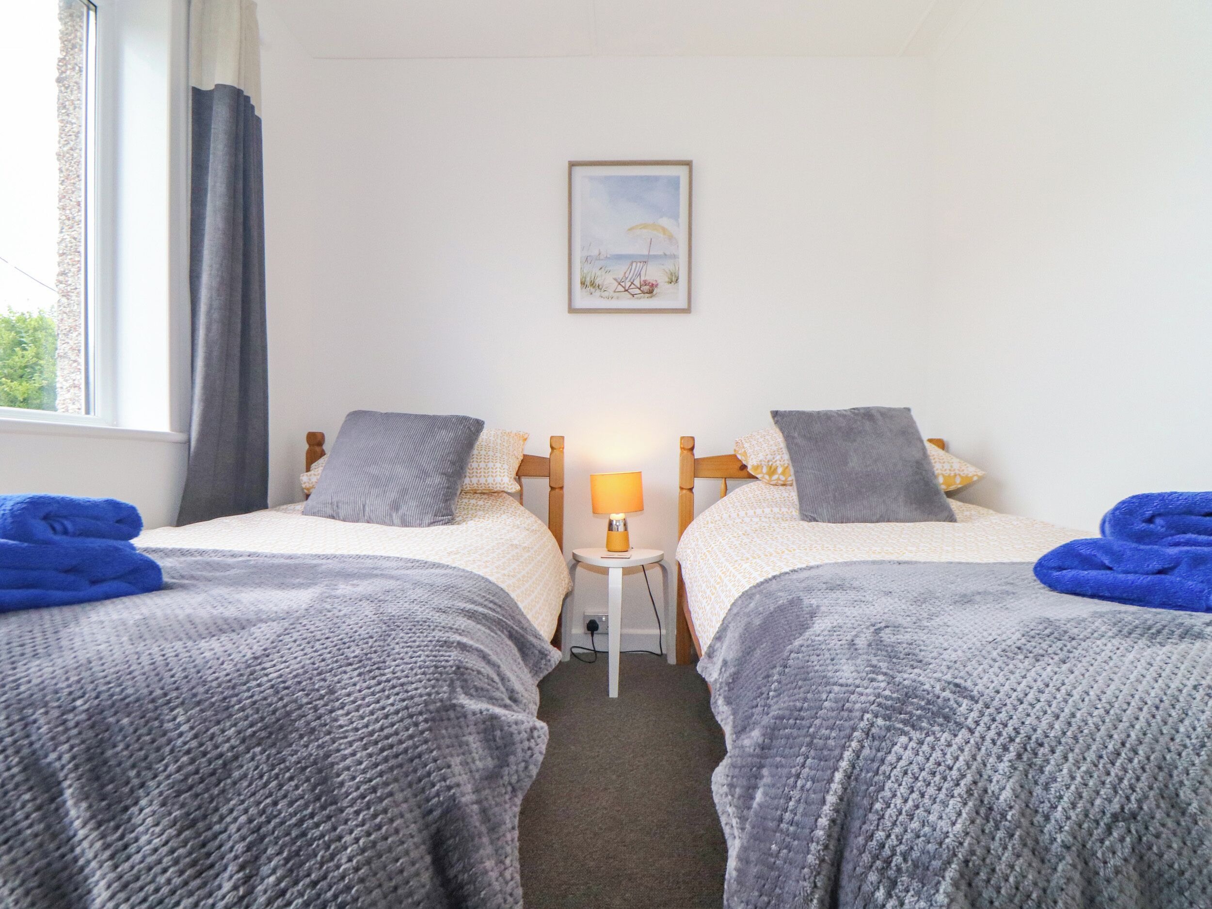 Et hotelværelse med to senge, et natbord, en lampe og et billede af en strand.