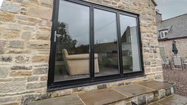 A stone building with a large black-framed sliding glass door. - Honeysuckle Cottage (Cornhill on Tweed)