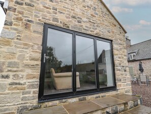 A stone building with a large black-framed sliding glass door. - Honeysuckle Cottage (Cornhill on Tweed)