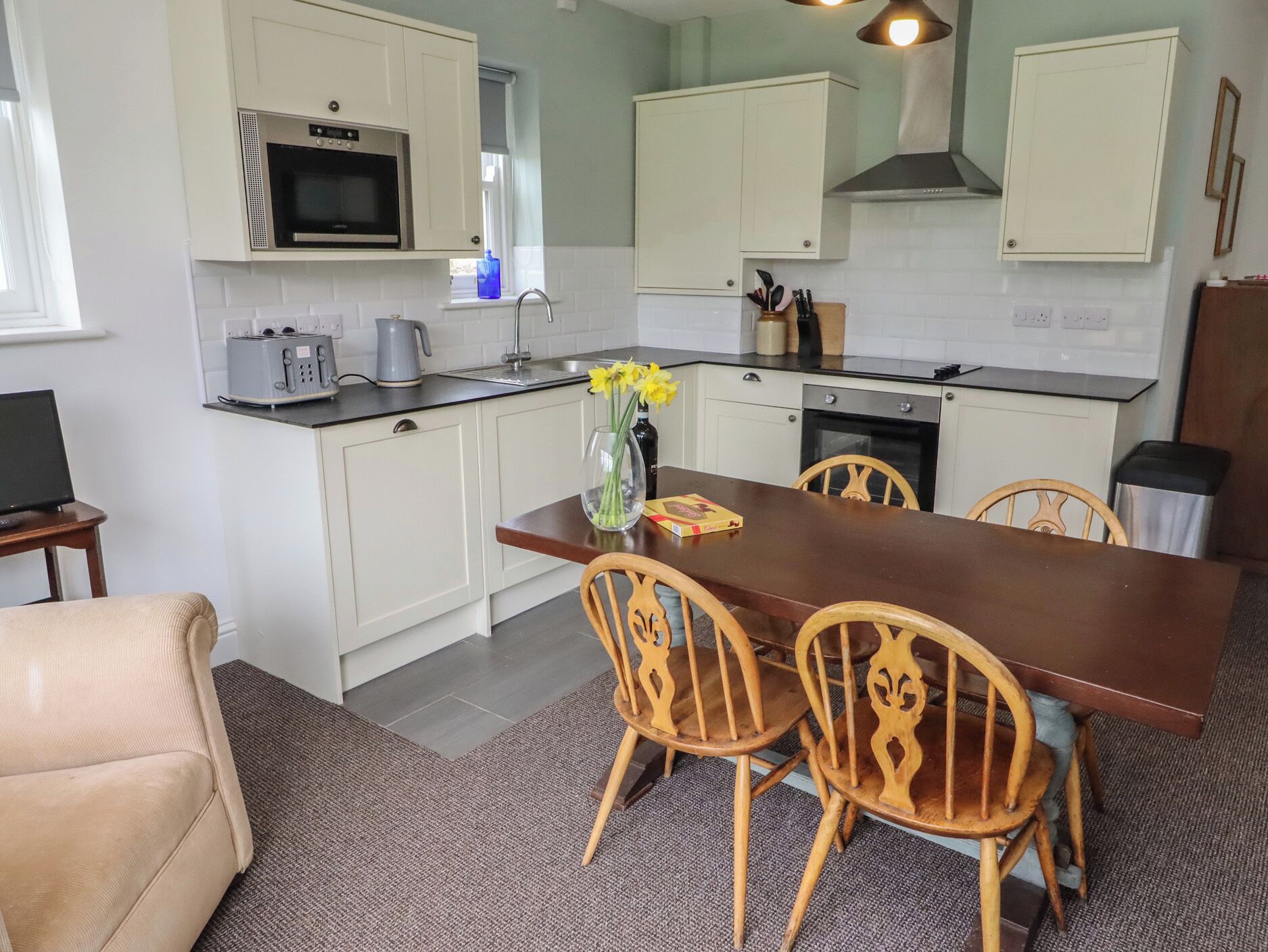 A compact kitchen with white cabinets, a microwave, a kettle, and a dining table with chairs.