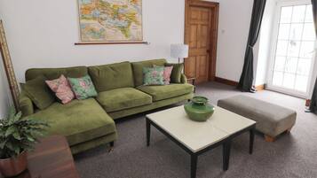 Un soggiorno con un divano verde, un tavolino da caffè, una mappa appesa al muro, una porta in legno e una finestra con tende.