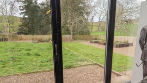 A view through a window of a garden with a wooden fence, gravel path, and greenery. - Honeysuckle Cottage (Cornhill on Tweed)