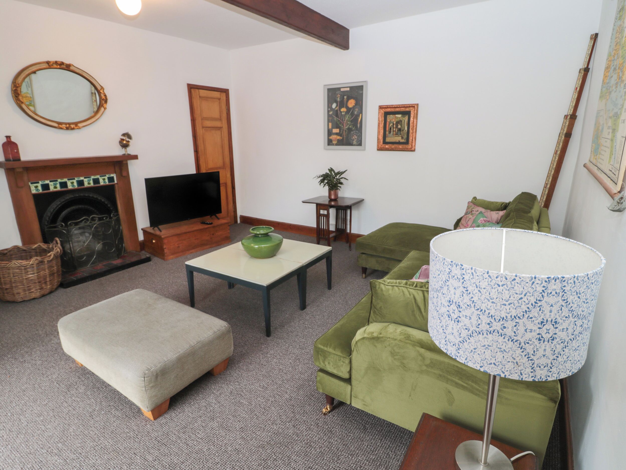 A living room with a fireplace, television, green sofa, ottoman, and a lamp.