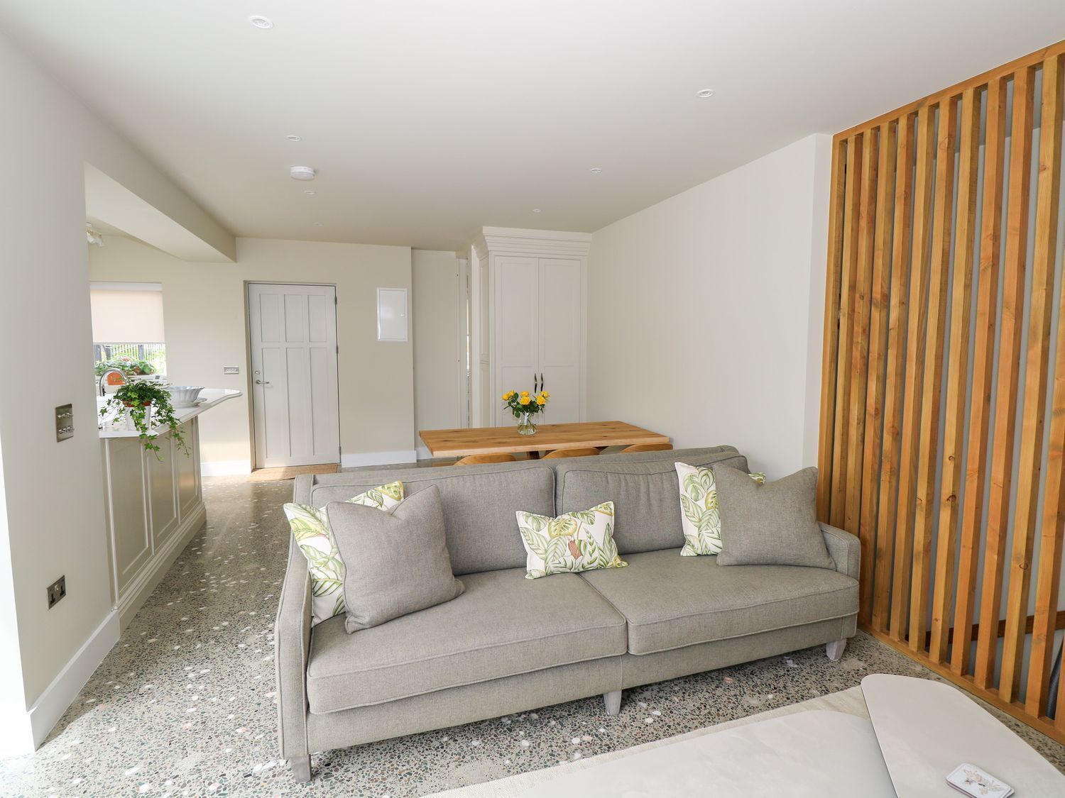 A modern living room with a grey sofa, a wooden partition, and a kitchen area in the background.