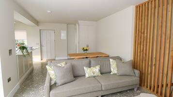 A modern living room with a grey sofa, a wooden partition, and a kitchen area in the background.