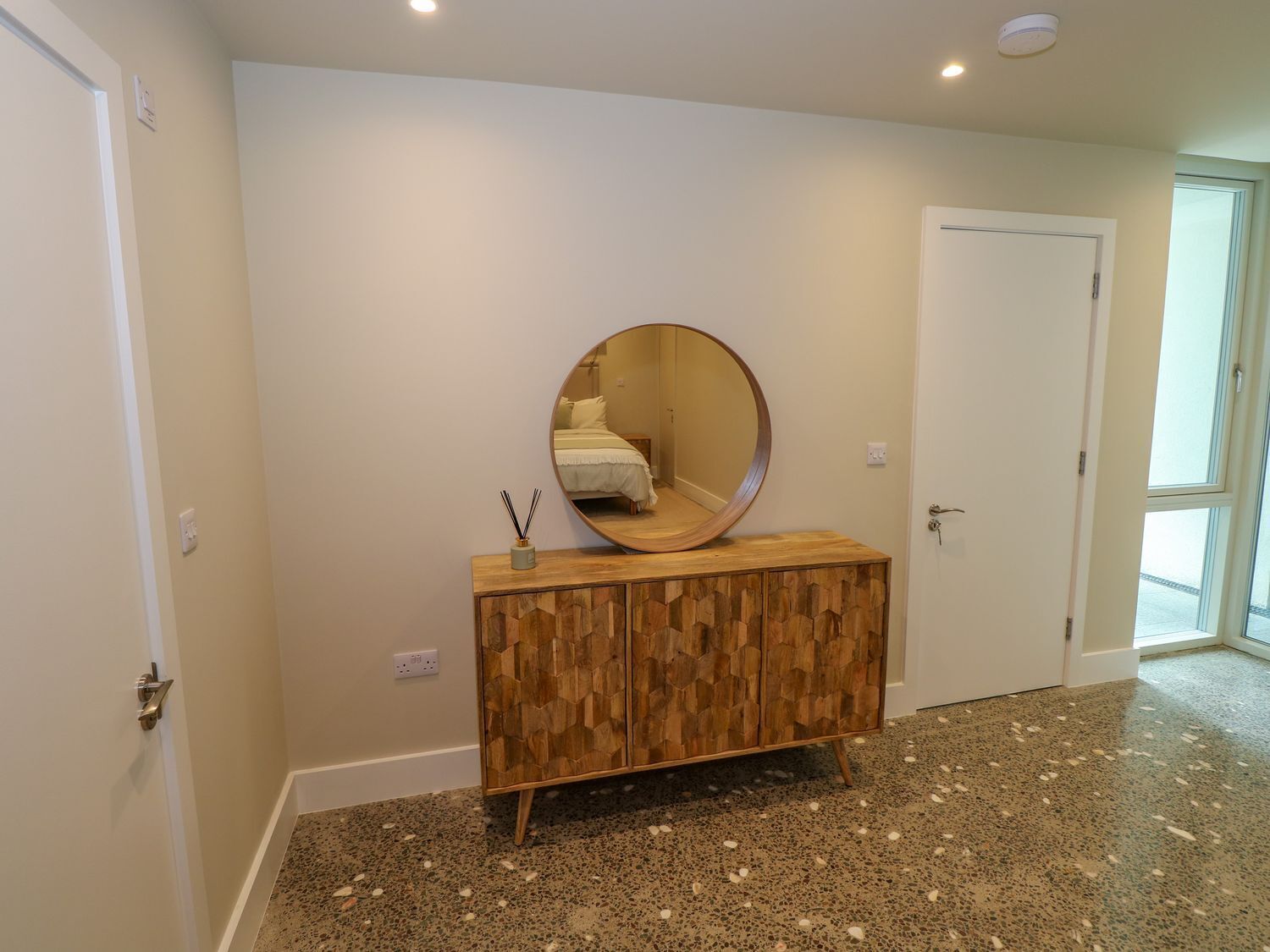 A hallway with a wooden cabinet, a round mirror, and a door.