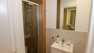 Une salle de bain avec une douche à parois de verre, un lavabo blanc avec un miroir et un mur carrelé.