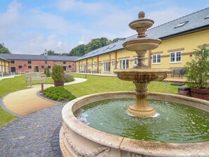 A courtyard with a stone fountain, a brick building, and a paved walkway. - Sandown Park Cottage (Oswestry)