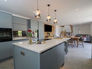 A modern kitchen with a central island, pendant lighting, and a dining area with a staircase. - The Hay Barn (Gloucester)