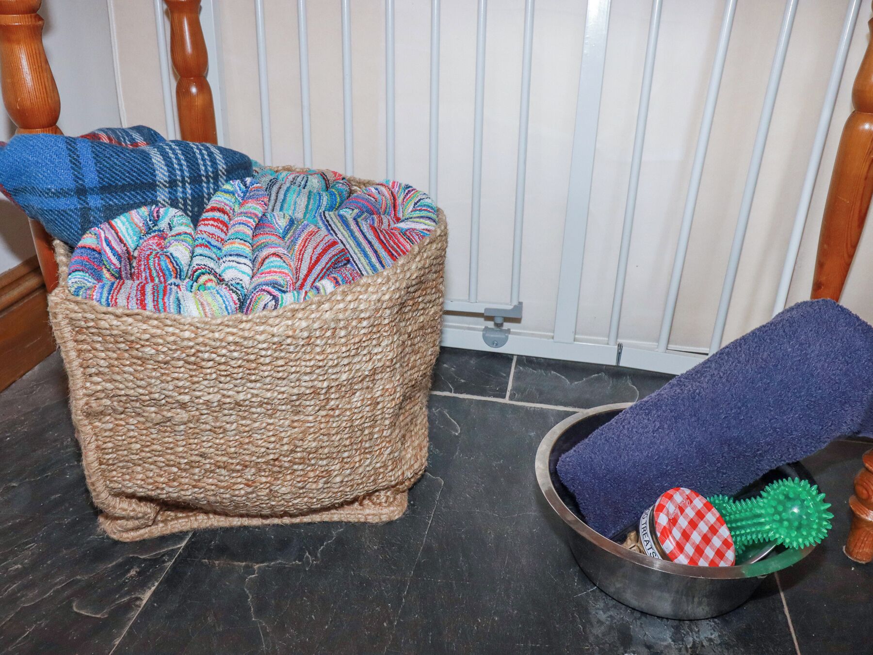 A woven basket with colorful blankets and a metal bowl with a blue towel and a green toy.