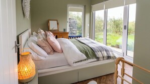 A bedroom with a bed, bedside table, lamp, and a view of the outdoors. - Tirlaggan House (Oban)