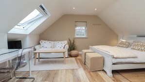 Ett modernt sovrum i loftstil med ett sluttande tak, ett takfönster, en stor säng, en soffa, ett skrivbord och en stol.