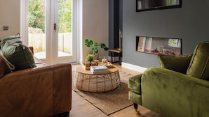Un salón con un sofá de cuero marrón, un sillón verde, una mesa de centro redonda de mimbre y una chimenea.