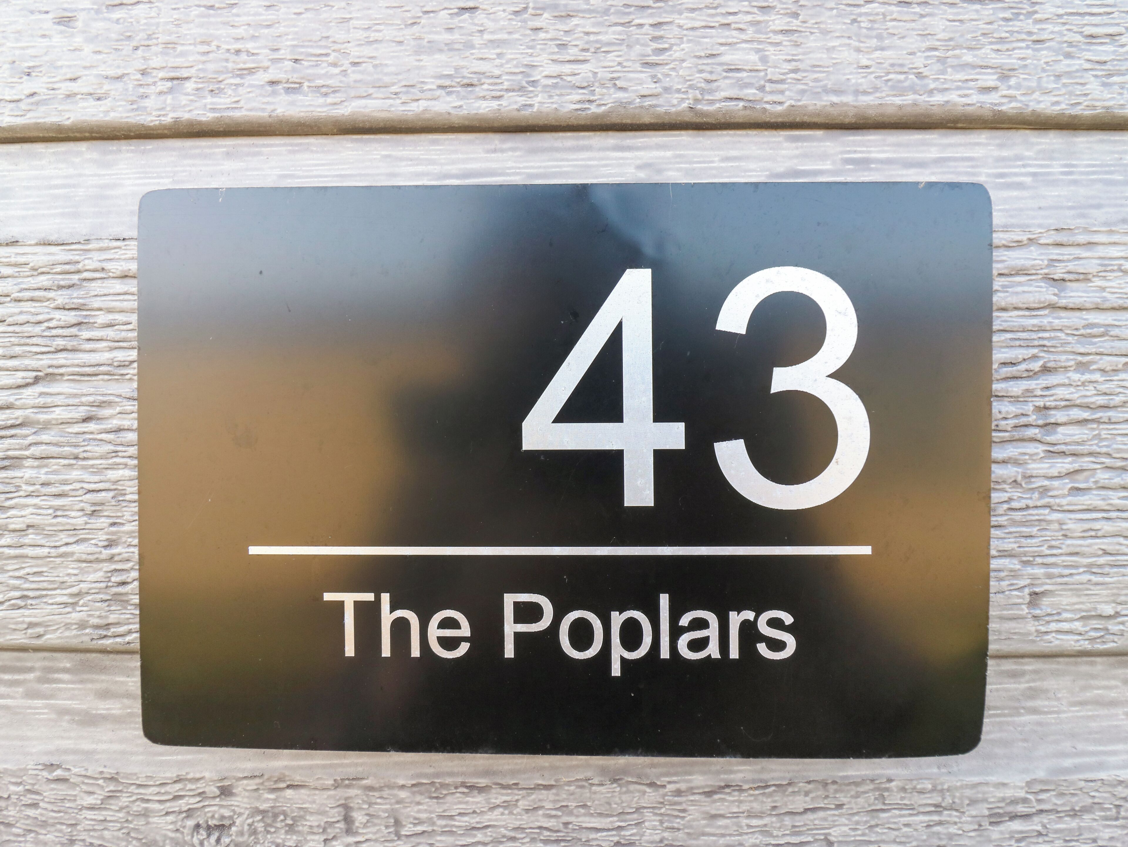 Uma placa preta com o número 43 e o texto 'The Poplars' em um fundo branco texturizado.