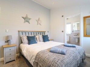 A bedroom with a bed, nightstands, a lamp, and a bathroom visible through an open door. - Number 43 The Poplars (King's Lynn)