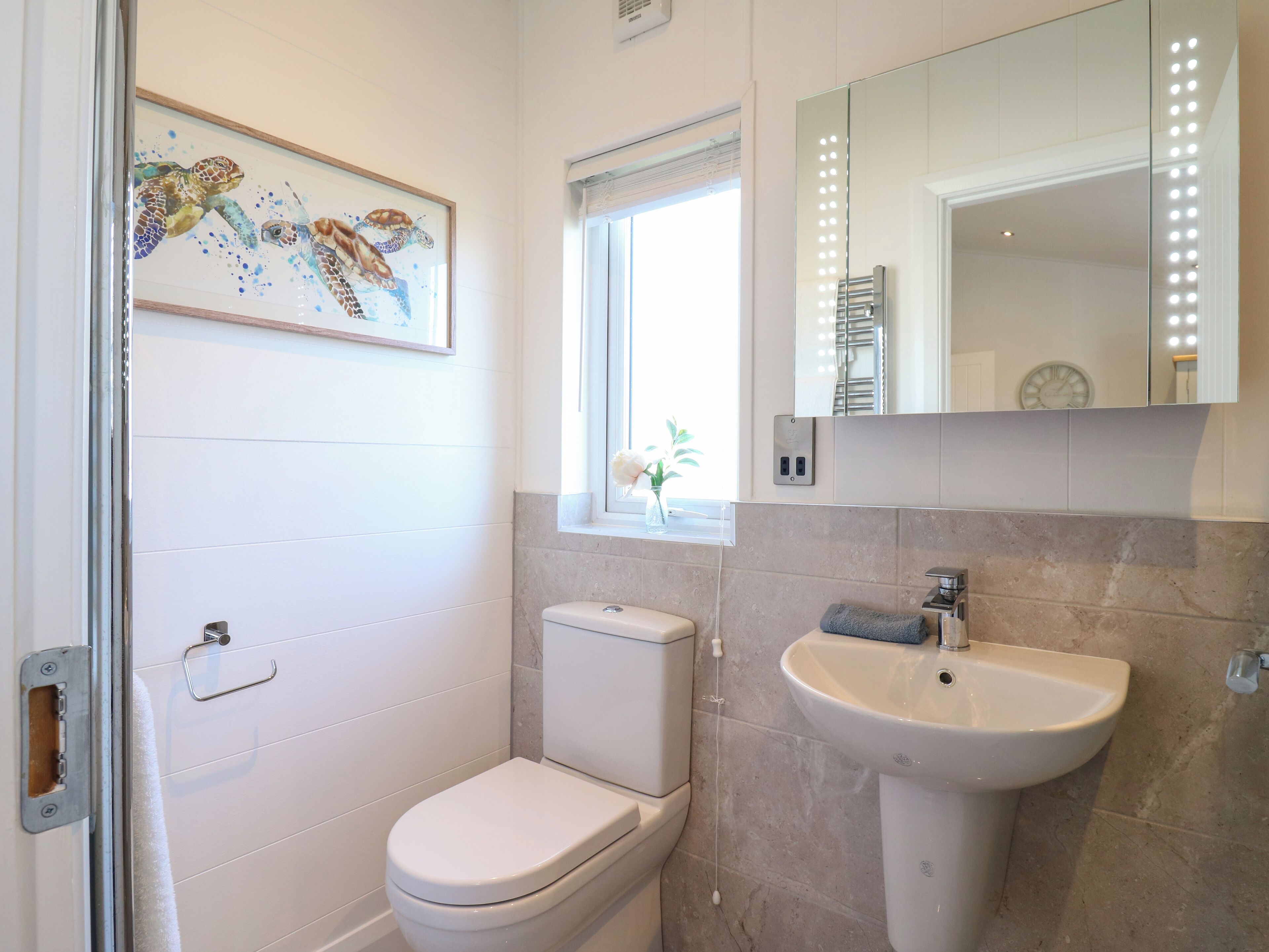 Een badkamer met toilet, wastafel en een kunstwerk in een lijst aan de muur.