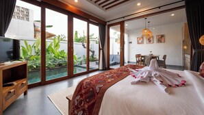 A bedroom with a large bed, a TV, and a sliding glass door leading to a balcony with plants. - Bila De Ubud Villas (Ubud)