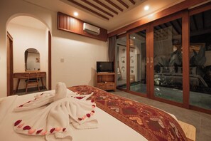 A bedroom with a large bed, a TV, a wooden cabinet, and a sliding glass door leading to a pool area. - Bila De Ubud Villas (Ubud)