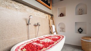 A bathroom with a freestanding bathtub filled with rose petals, a shower area, and decorative shelves. - Bila De Ubud Villas (Ubud)