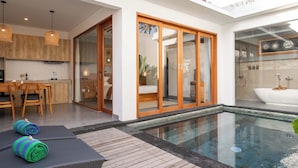 A modern outdoor pool area with a wooden deck, a glass-enclosed shower, and a dining area with wooden furniture. - Bila De Ubud Villas (Ubud)