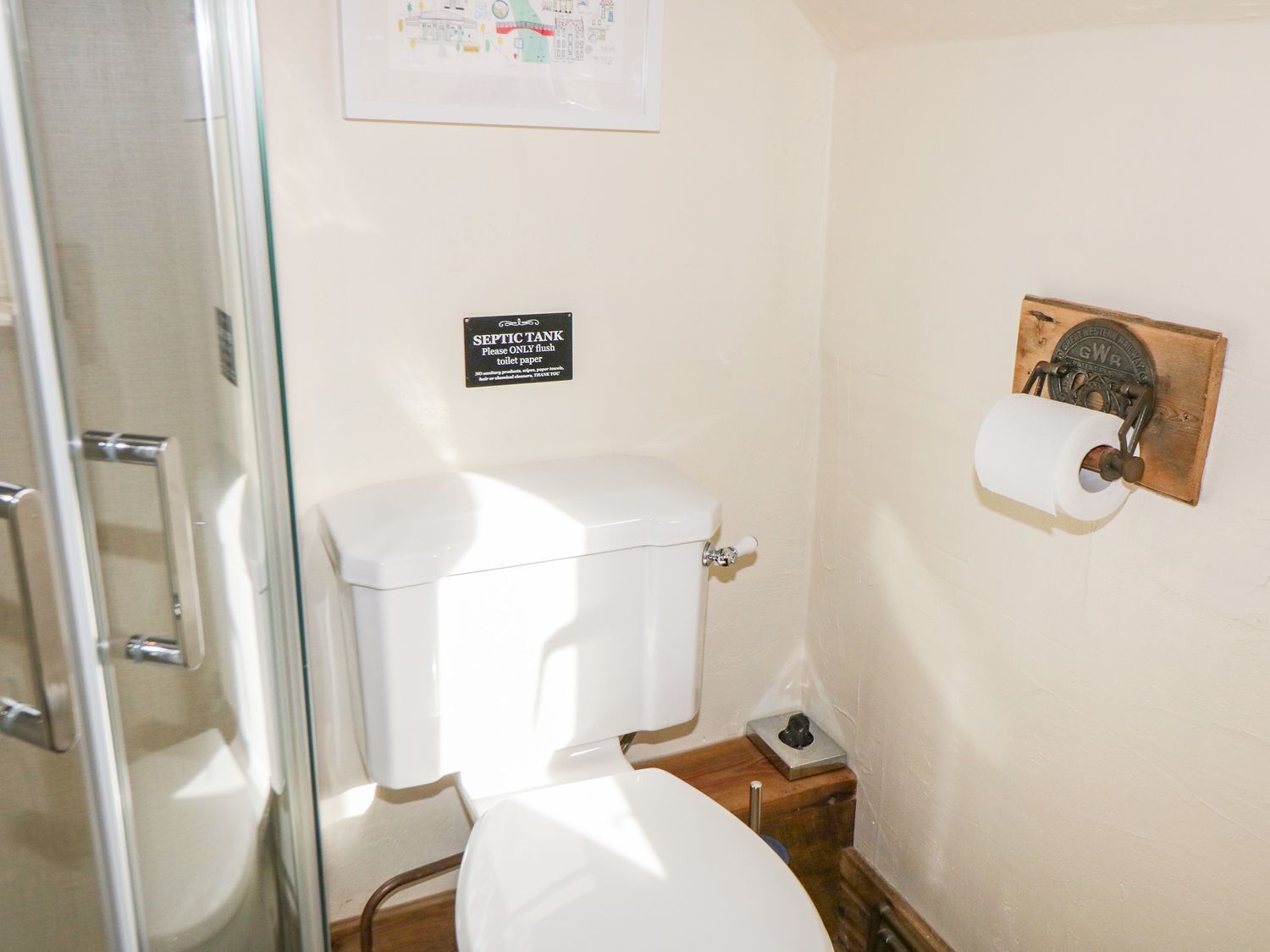 Une salle de bain équipée de toilettes, d’un porte-rouleau en bois et d’un panneau indiquant l’emplacement de la fosse septique.