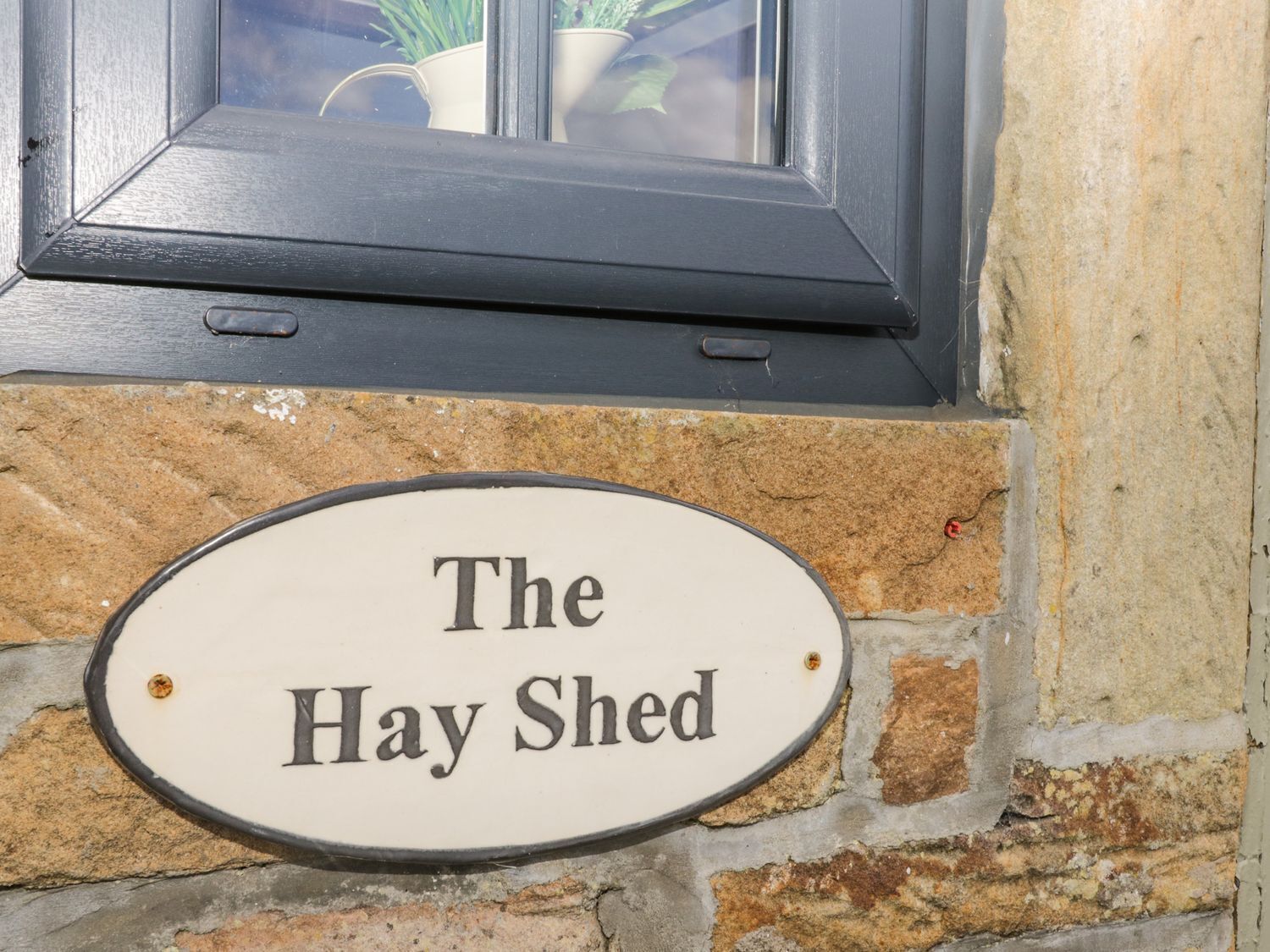 Un cartello con la scritta 'The Hay Shed' fissato a un muro in pietra.