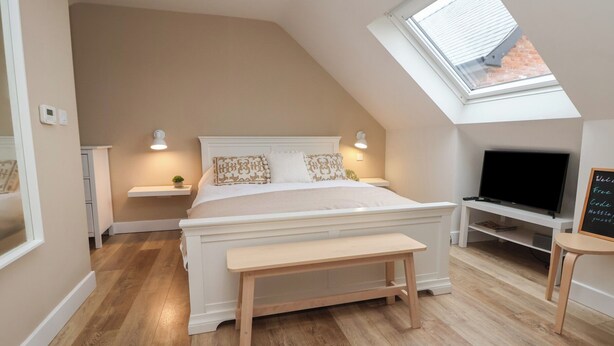 A bedroom with a sloped ceiling, a bed, a TV, and a skylight. - Nettleford Inhale (Tarporley)