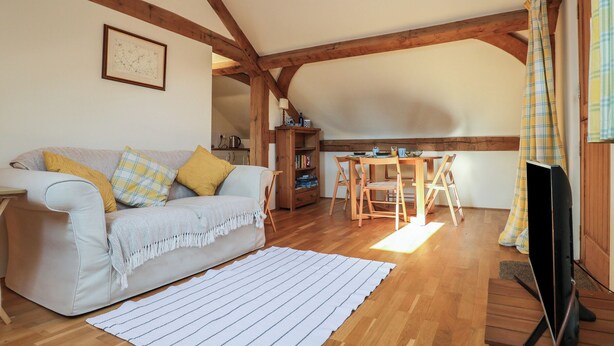 A cozy living room with a sofa, wooden beams, a dining table, and a television.