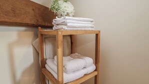 A wooden shelf with neatly folded white towels and a small white flower arrangement.