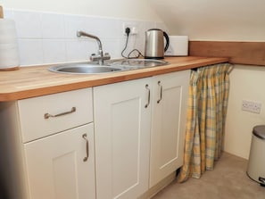 Una cocina con un lavabo, una tetera y un tostador sobre la encimera.