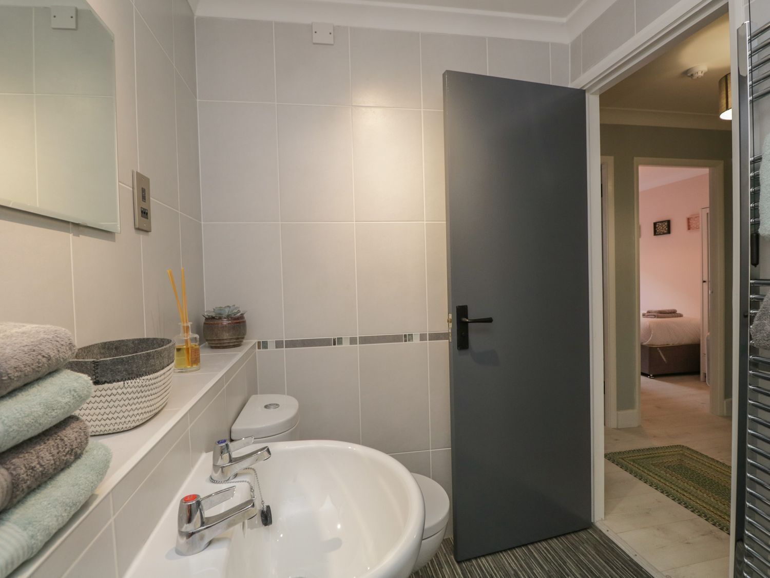 A bathroom with a white sink, a toilet, and a dark door leading to a bedroom.