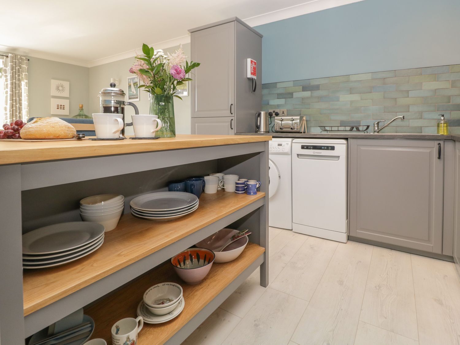 Une cuisine moderne avec des meubles gris, un plan de travail en bois et un lave-vaisselle.