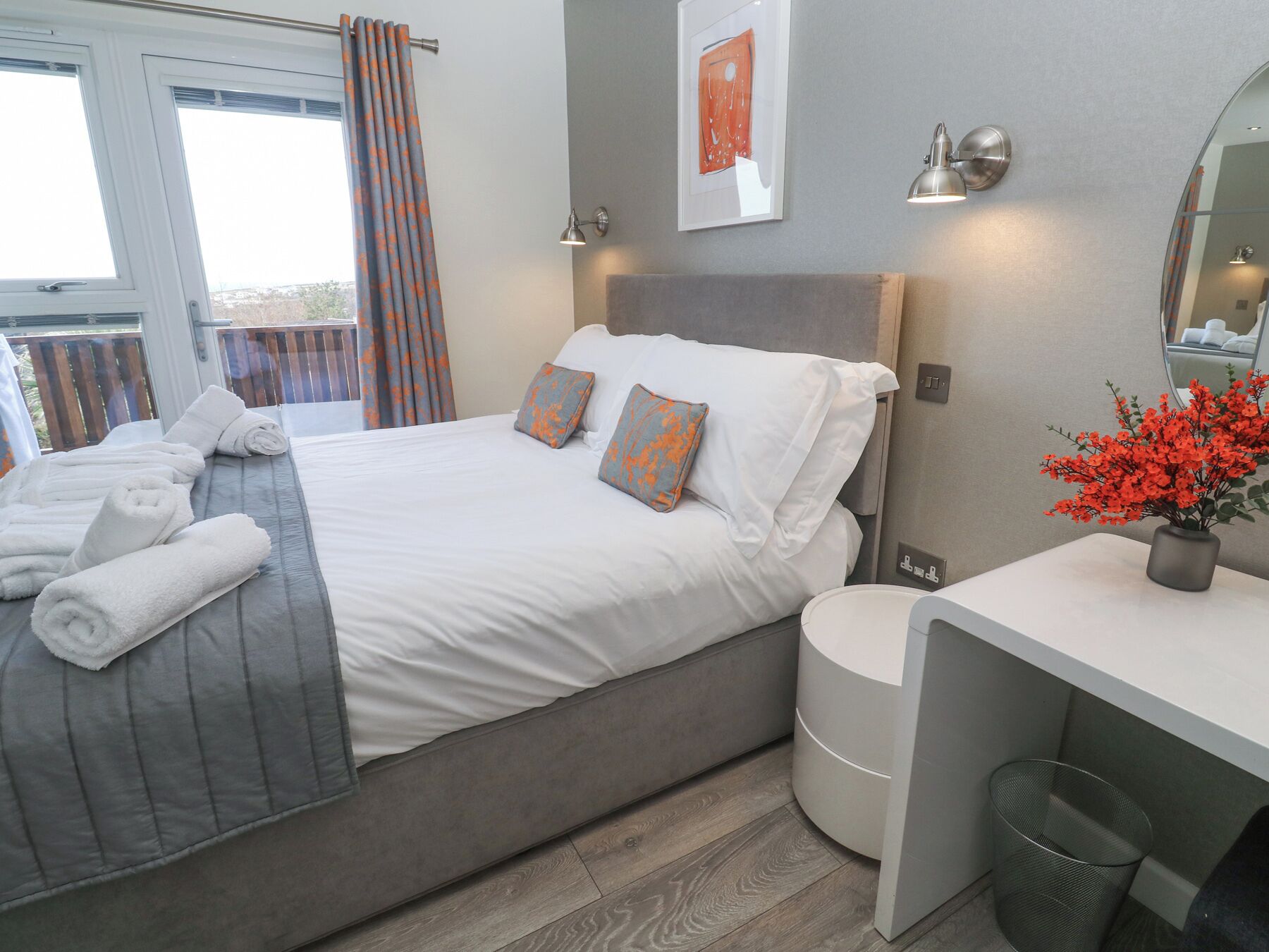 Habitación de hotel con cama, mesita de noche, espejo, planta en maceta y ventana con cortinas.