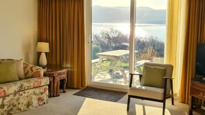 Una habitación con sofá, una silla, una mesita con lámpara y vistas a un lago a través de un ventanal corredero.