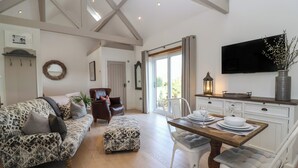 A spacious living area with a patterned sofa, a dining table set for four, and a television mounted on the wall. - Church View Retreat (Weston-super-Mare)