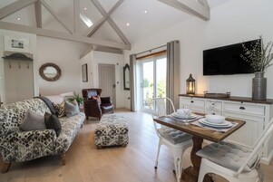 A spacious living area with a patterned sofa, a dining table set for four, and a television mounted on the wall.