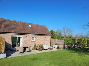 A brick house with a tiled roof, a door, and a small window. There is a patio with outdoor furniture and potted plants. - Church View Retreat (Weston-super-Mare)